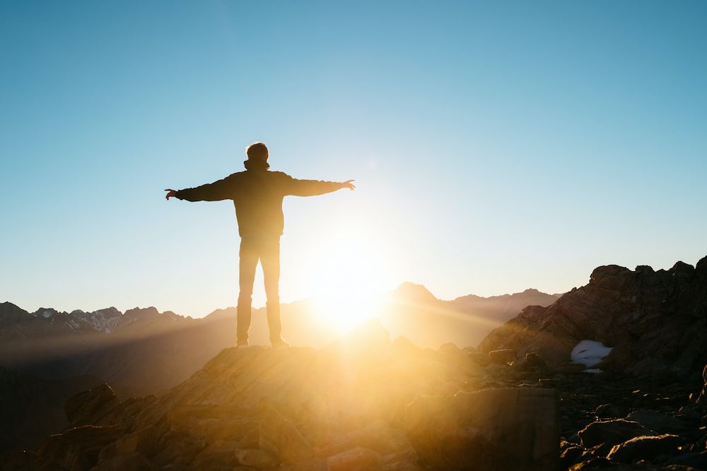 Man stands on mountain praising God in faith.